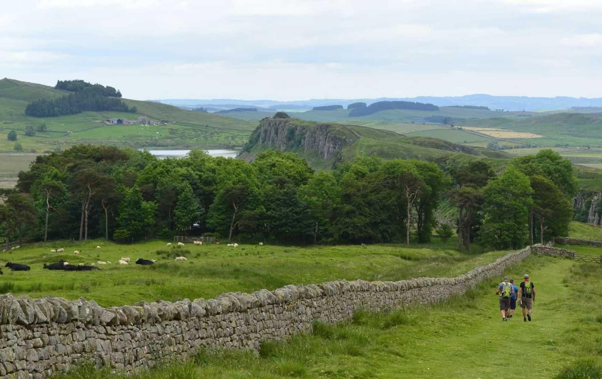 Walkers following Hadrian’s Wall across Northumberland farmland towards the Whin Sill ridge