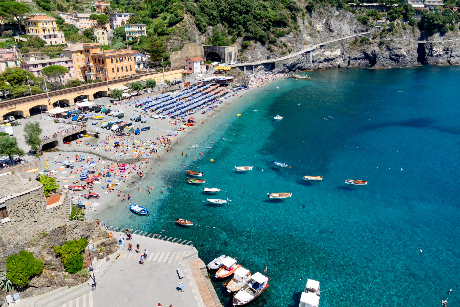 Monterosso beach and bay, with fishing boats and steep coastal cliffs beyond.