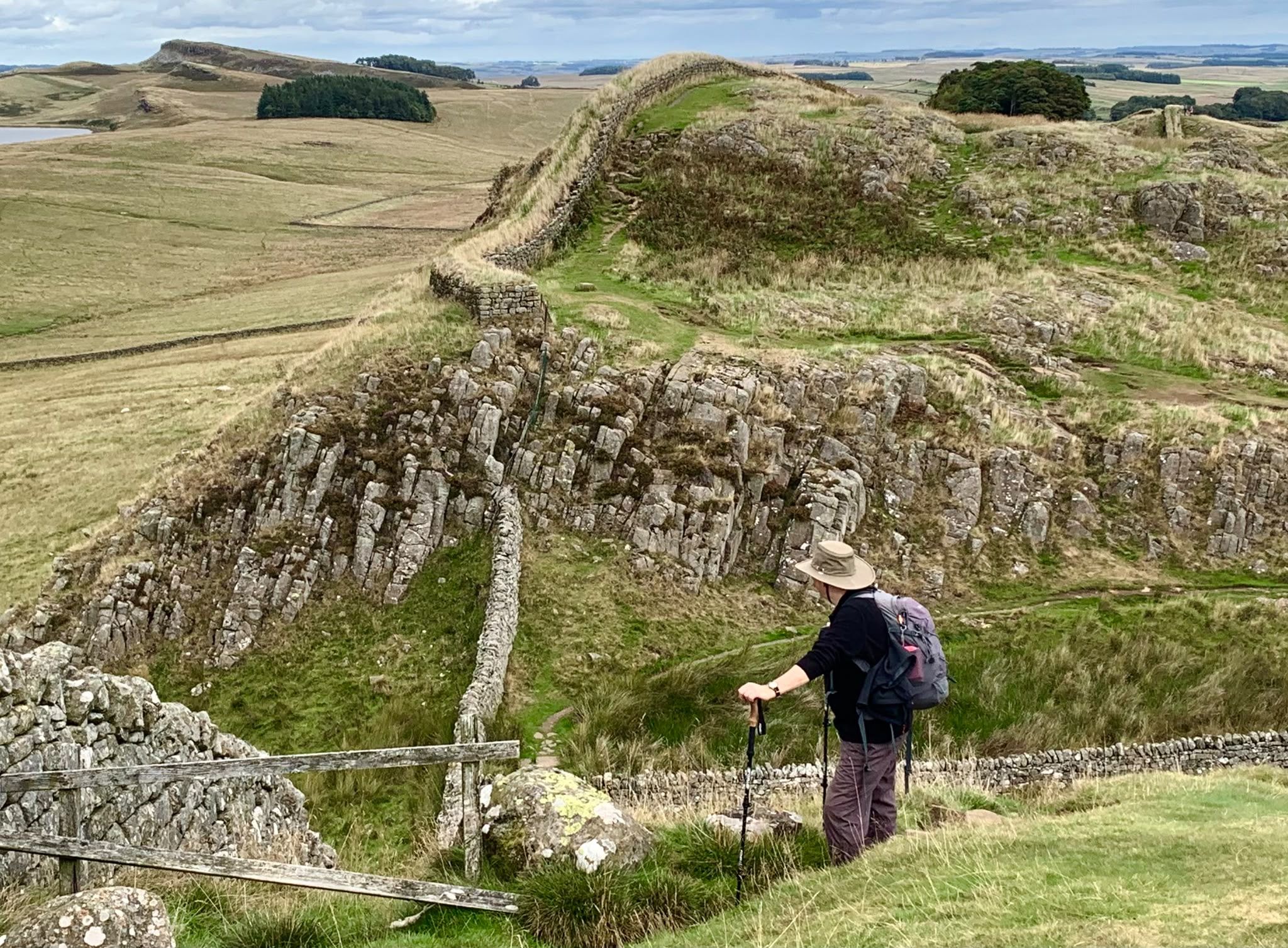 Walker beside Hadrian’s Wall, looking across the rocky crags and open countryside.
