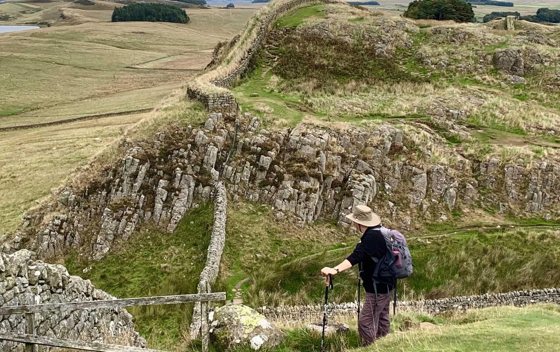 Walker beside Hadrian’s Wall, looking across the rocky crags and open countryside.