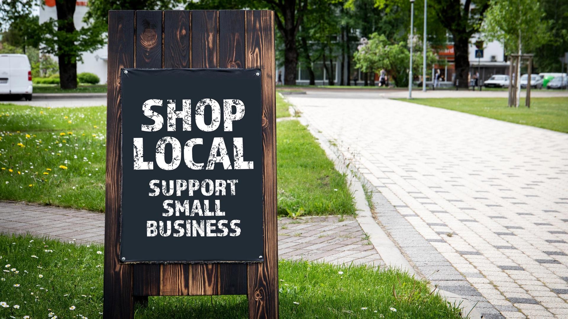 A wooden A-frame sign with a chalkboard displays the message "SHOP LOCAL SUPPORT SMALL BUSINESS" in white lettering.