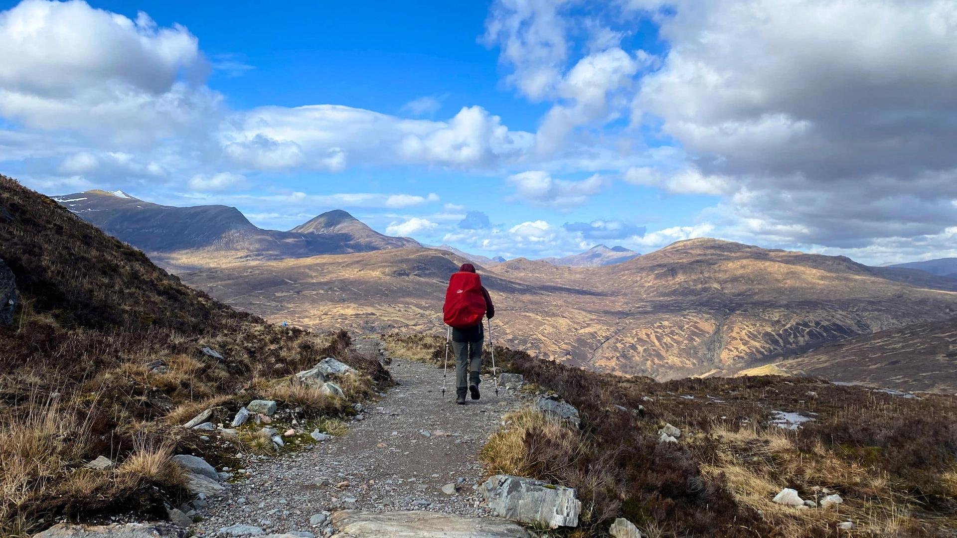 west highland way trail, with Holly Robertson walking on the trail with a red backpack and walking poles.