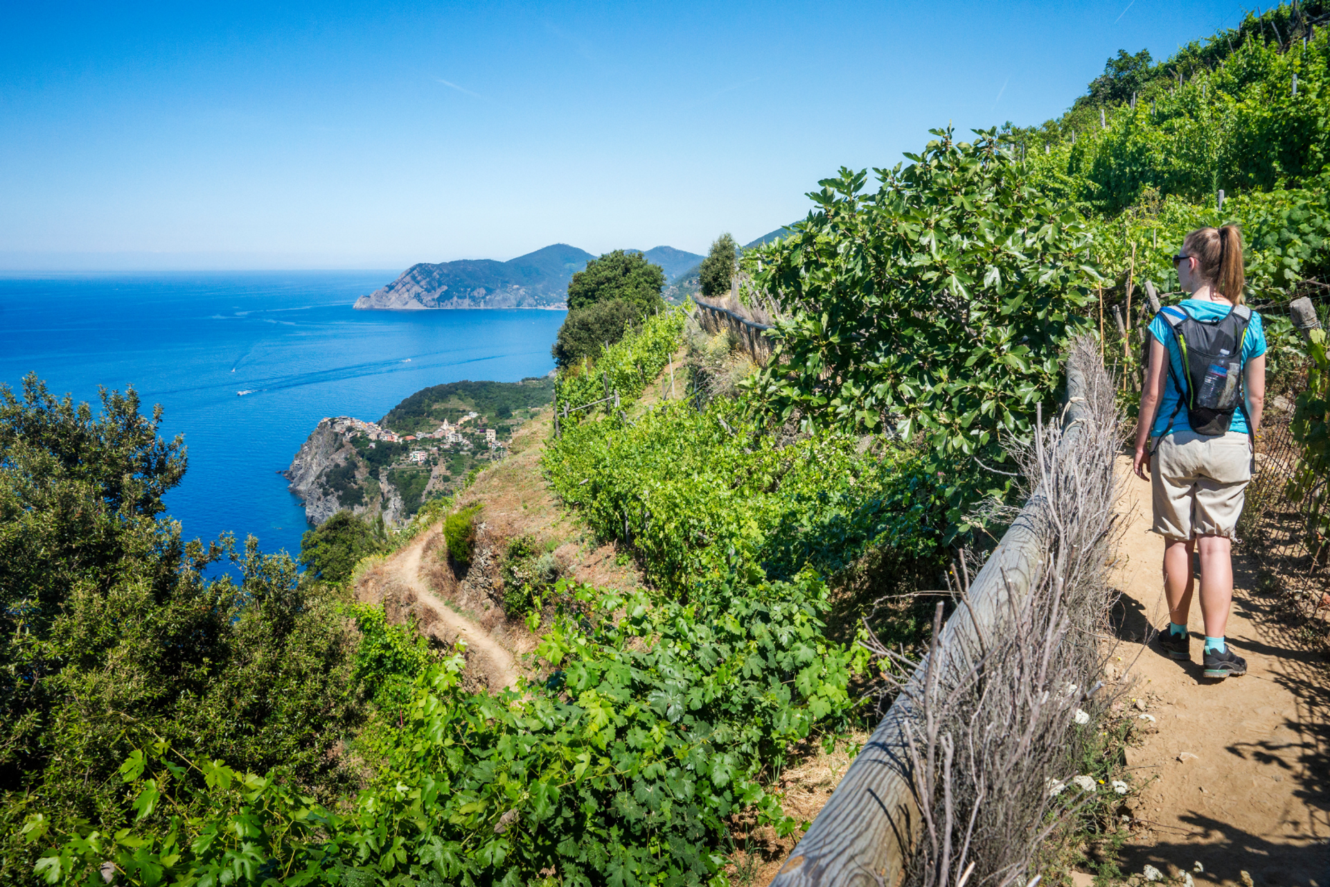 Walker following a narrow coastal path above the Ligurian Sea.