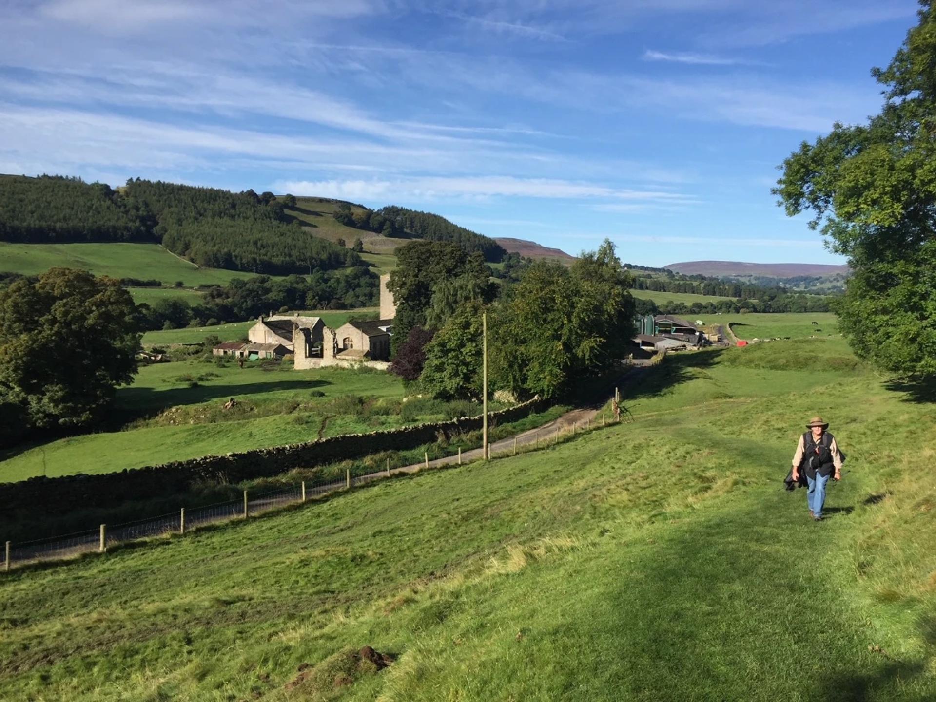 Walker descending through green countryside near Richmond on the Coast to Coast Walk