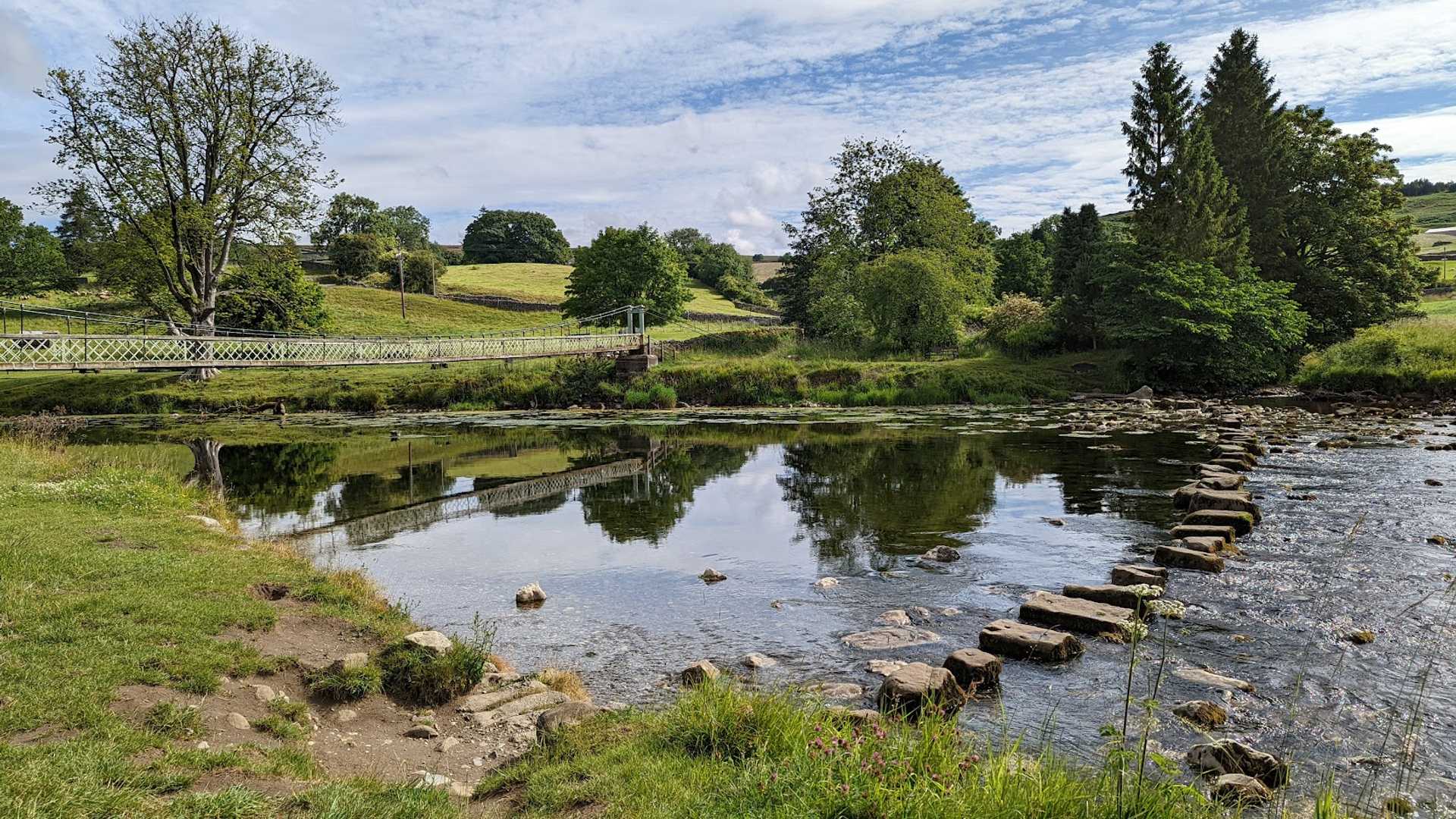 Walker crossing a suspension bridge on the Dales Way in the Yorkshire Dales