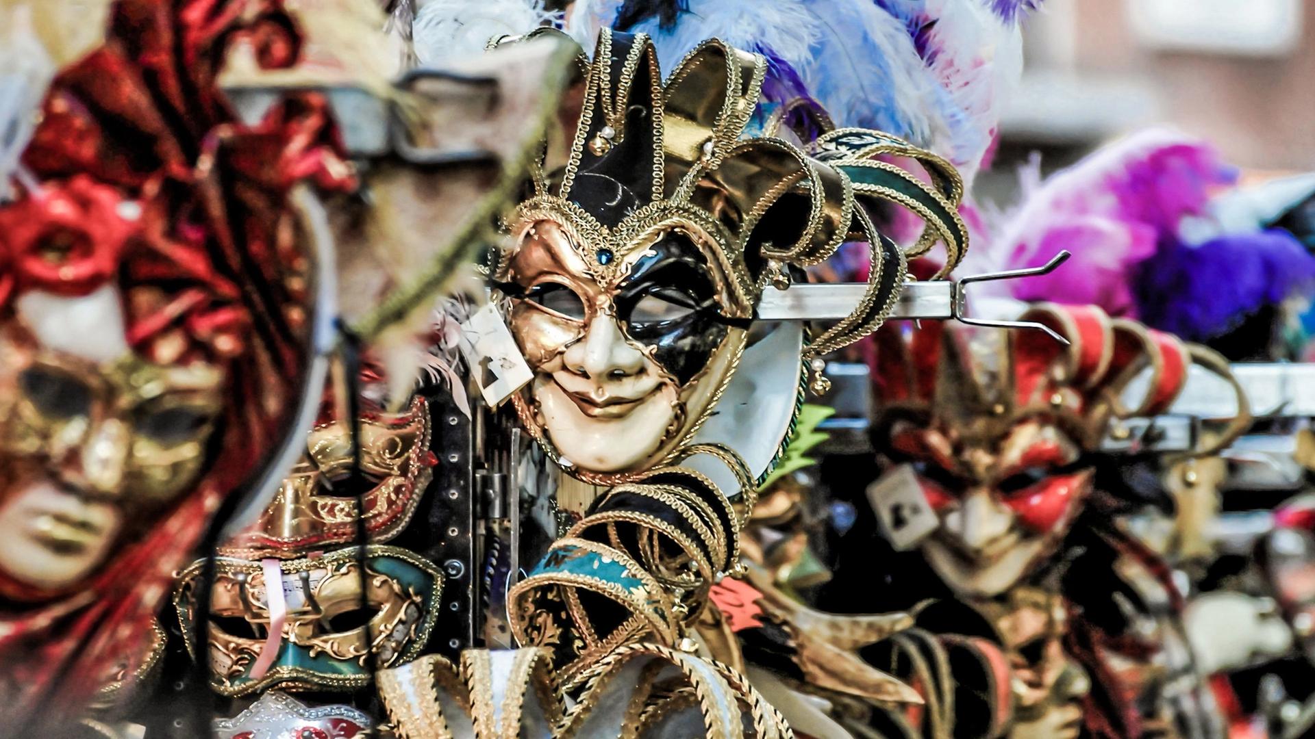 A display of ornate Venetian masks in various colours and styles, featuring jester masks and feathered embellishments.