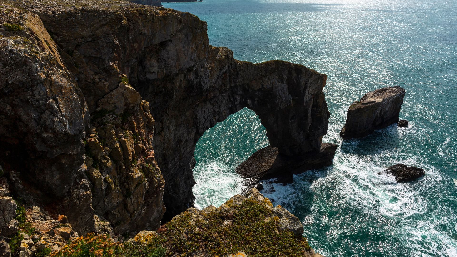 Green Bridge of Wales sea arch on the Pembrokeshire coast, with waves and rock stacks.