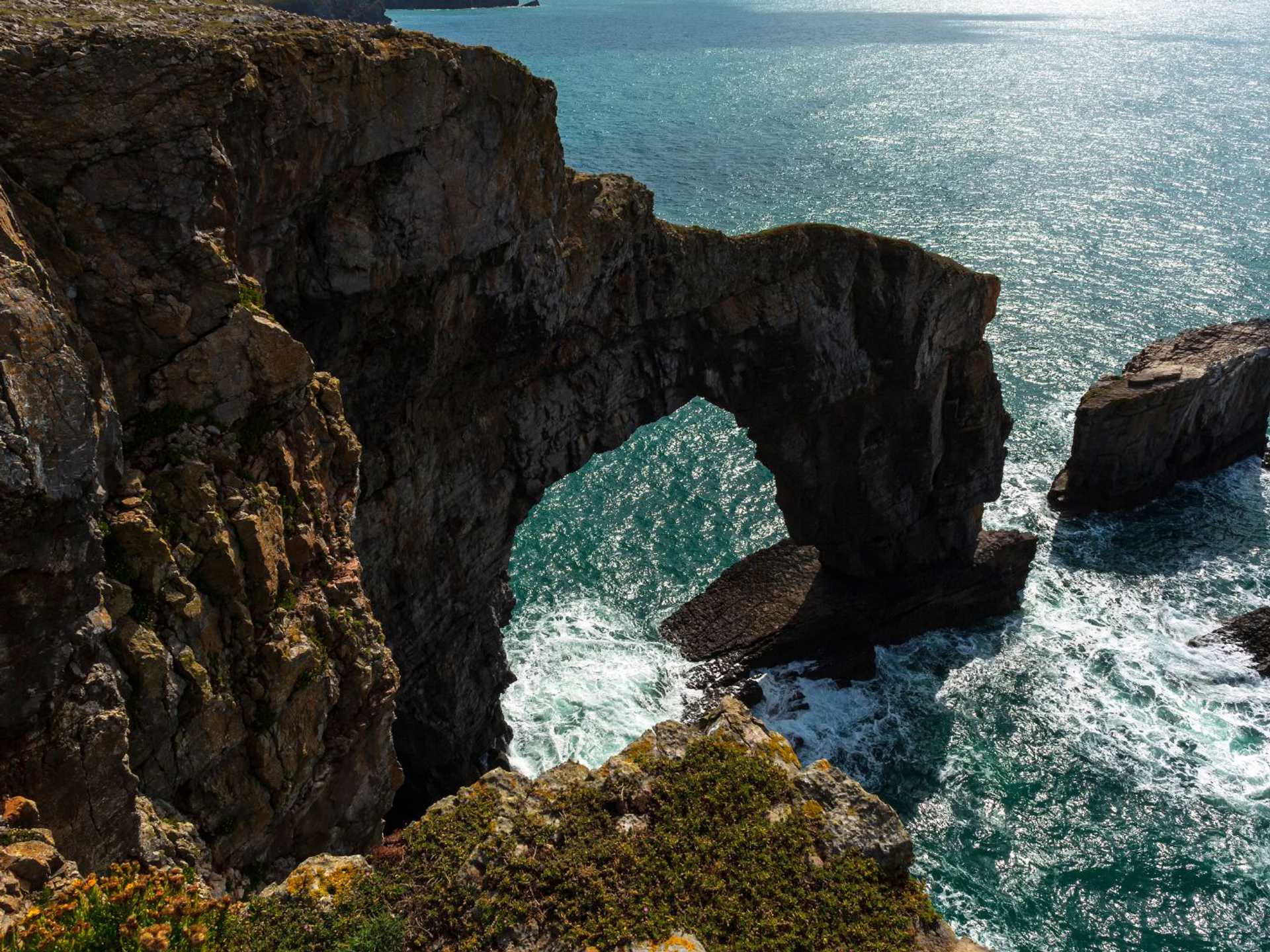 Green Bridge of Wales sea arch on the Pembrokeshire coast, with waves and rock stacks.