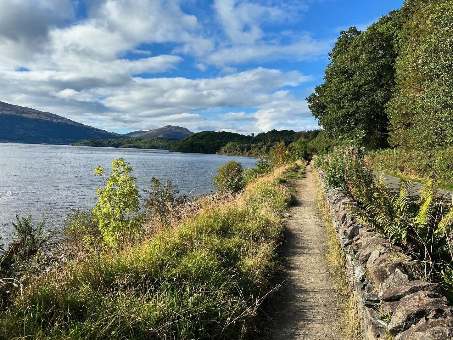 Narrow West Highland Way path following the eastern shore of Loch Lomond, with hills beyond.