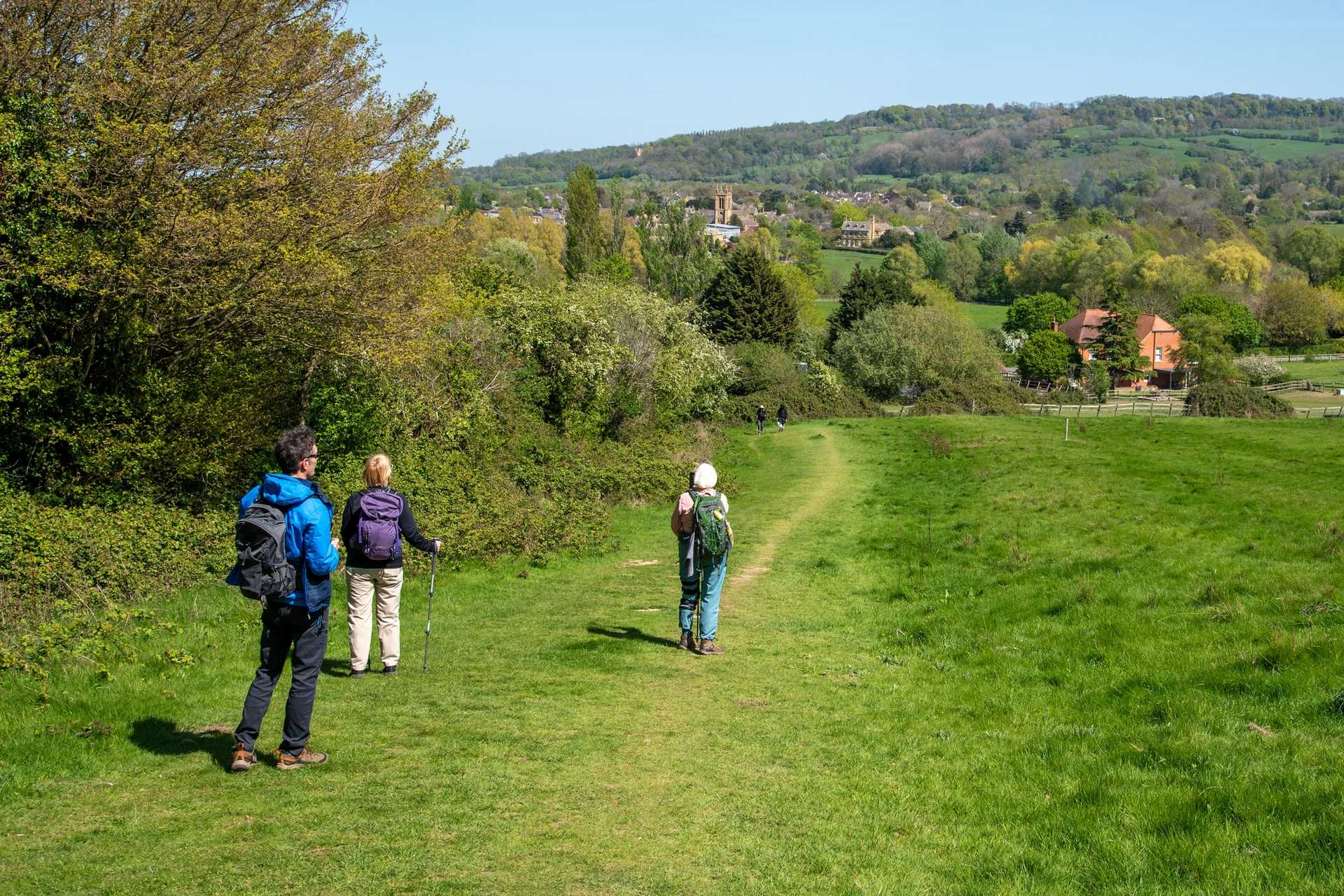 Walkers hiking through lush green grass in Cotswolds