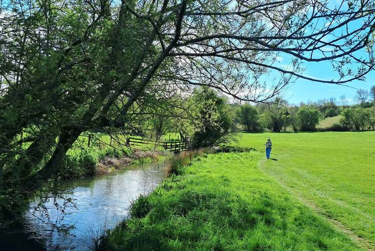 Walker following a quiet riverside path through green countryside on a self-guided walking holiday.