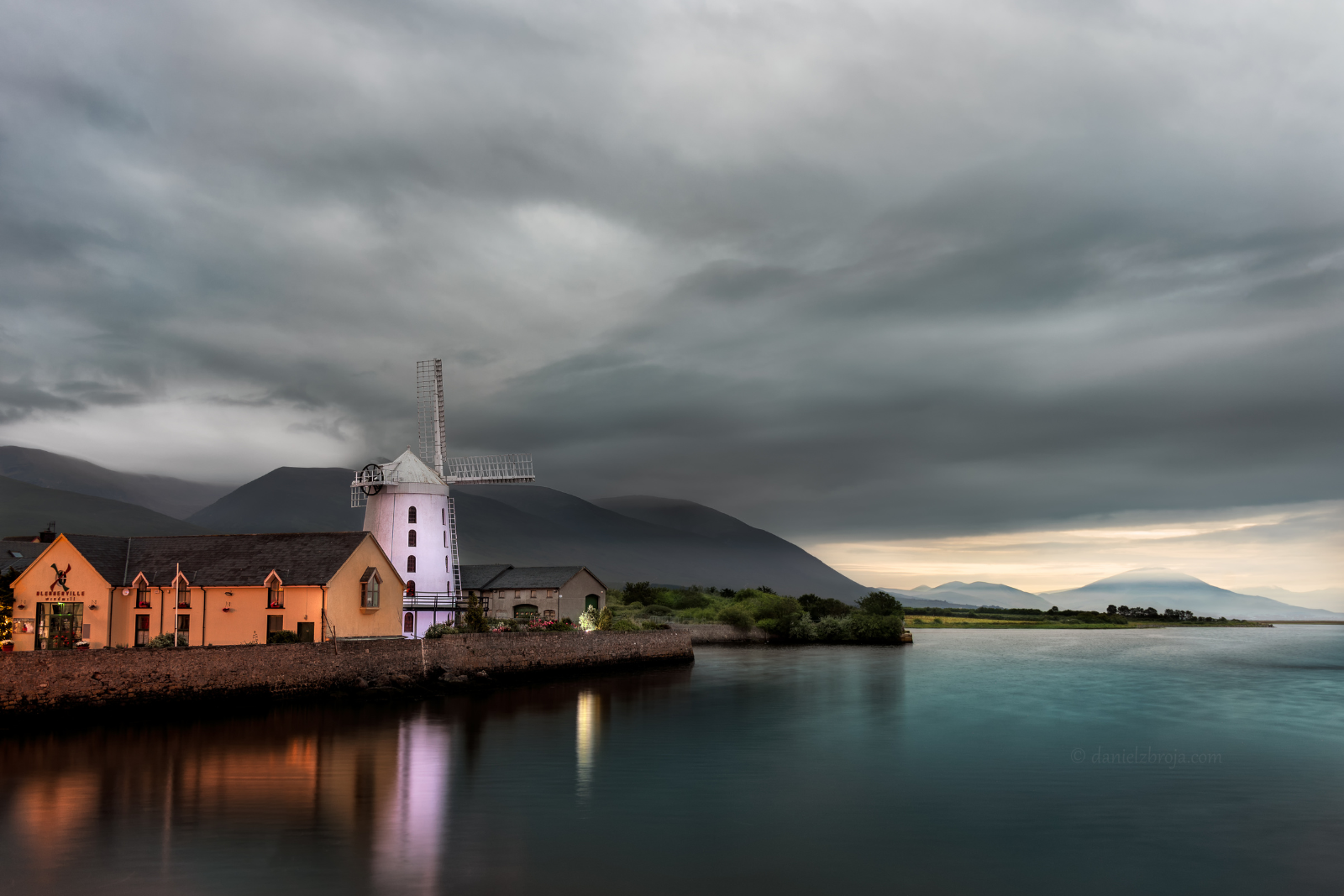 Blennerville Windmill beside the water near Tralee beneath a cloudy sky.