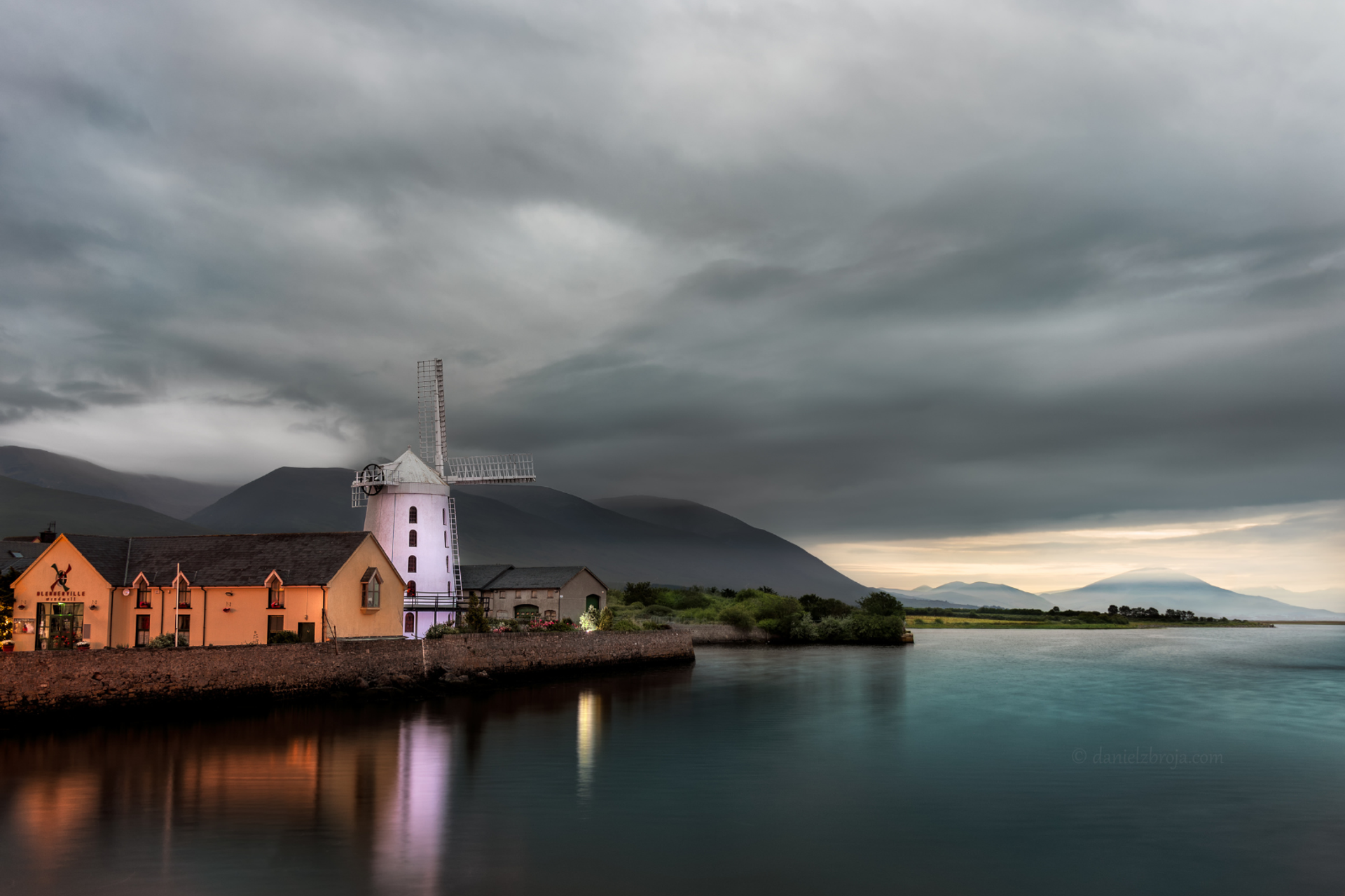 Blennerville Windmill beside the water near Tralee beneath a cloudy sky.