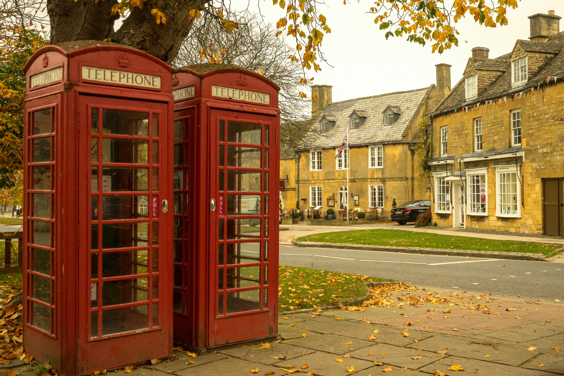 Two traditional red telephone boxes beside honey-coloured Cotswold stone buildings in Broadway.