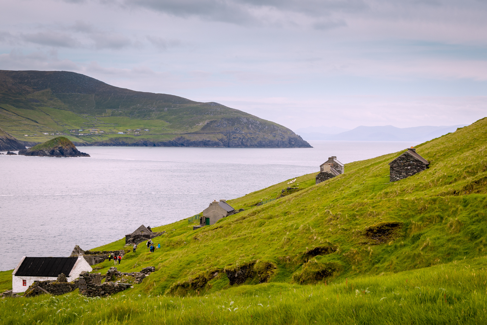 Stone cottages scattered across a green hillside overlooking the sea and distant mountains.