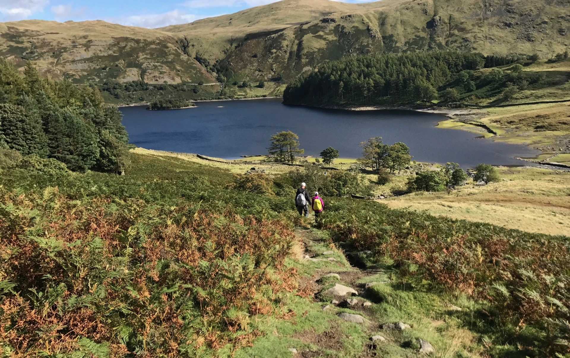 Walkers descending towards a mountain lake in the Lake District on the Coast to Coast Walk