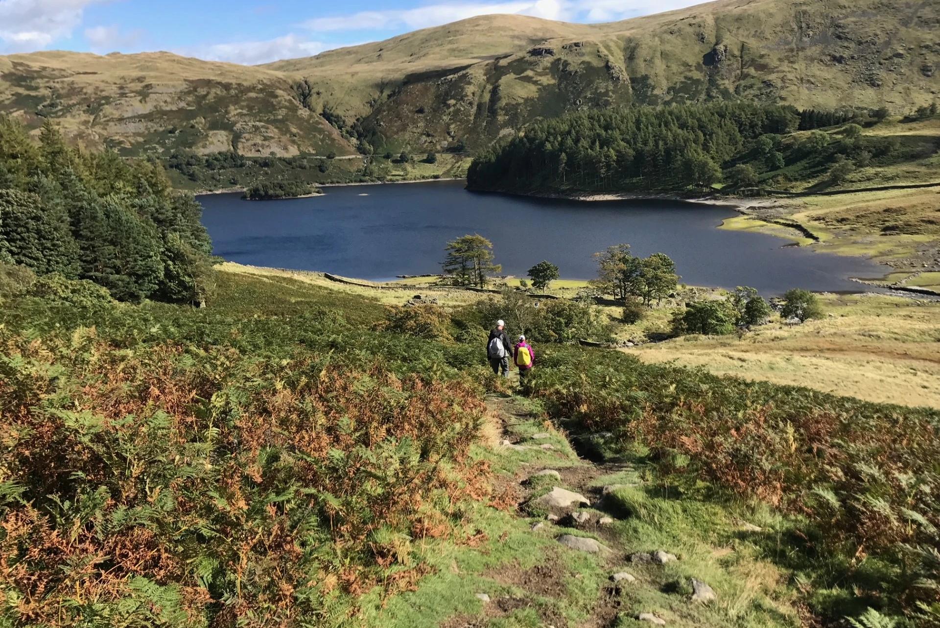 Walkers descending towards a mountain lake in the Lake District on the Coast to Coast Walk