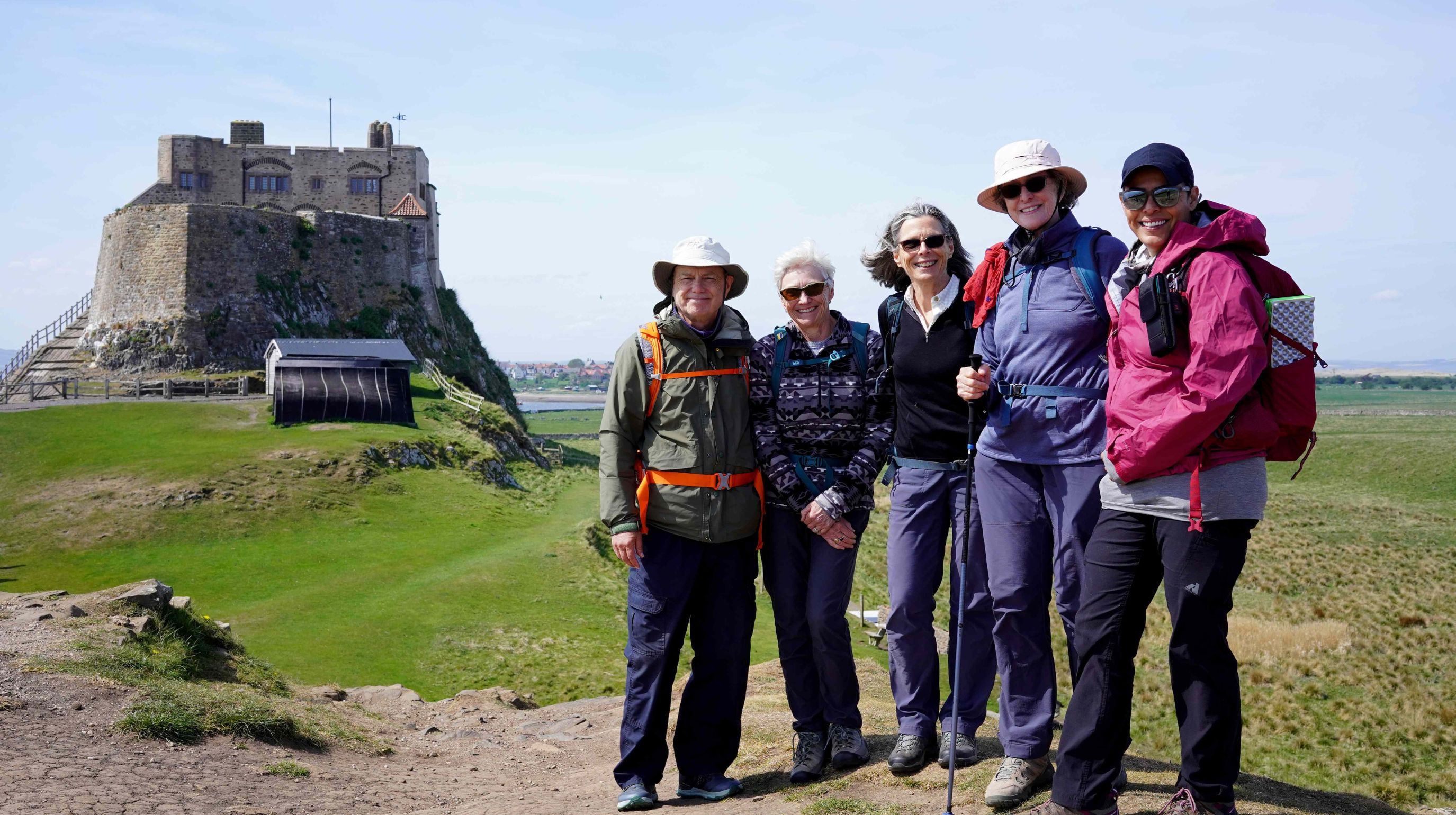 Five hikers stand on a hill with a stone castle behind them under a clear blue sky.