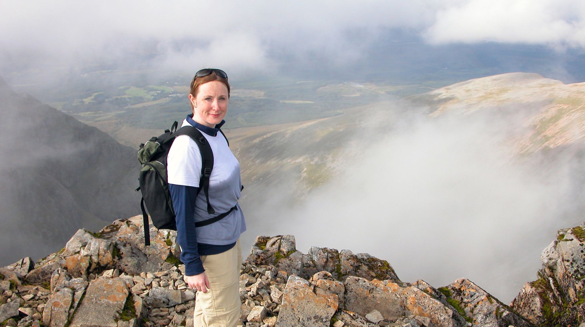 A person stands on a rocky mountain peak with clouds obscuring the valley below.