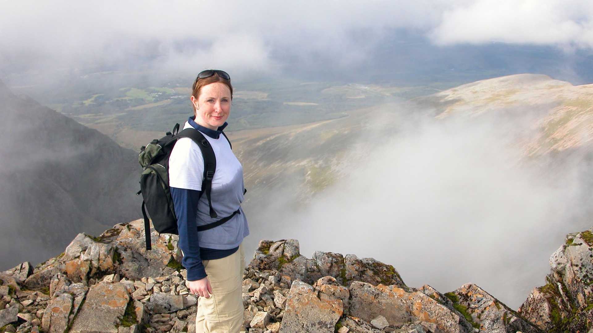 A person stands on a rocky mountain peak with clouds obscuring the valley below.