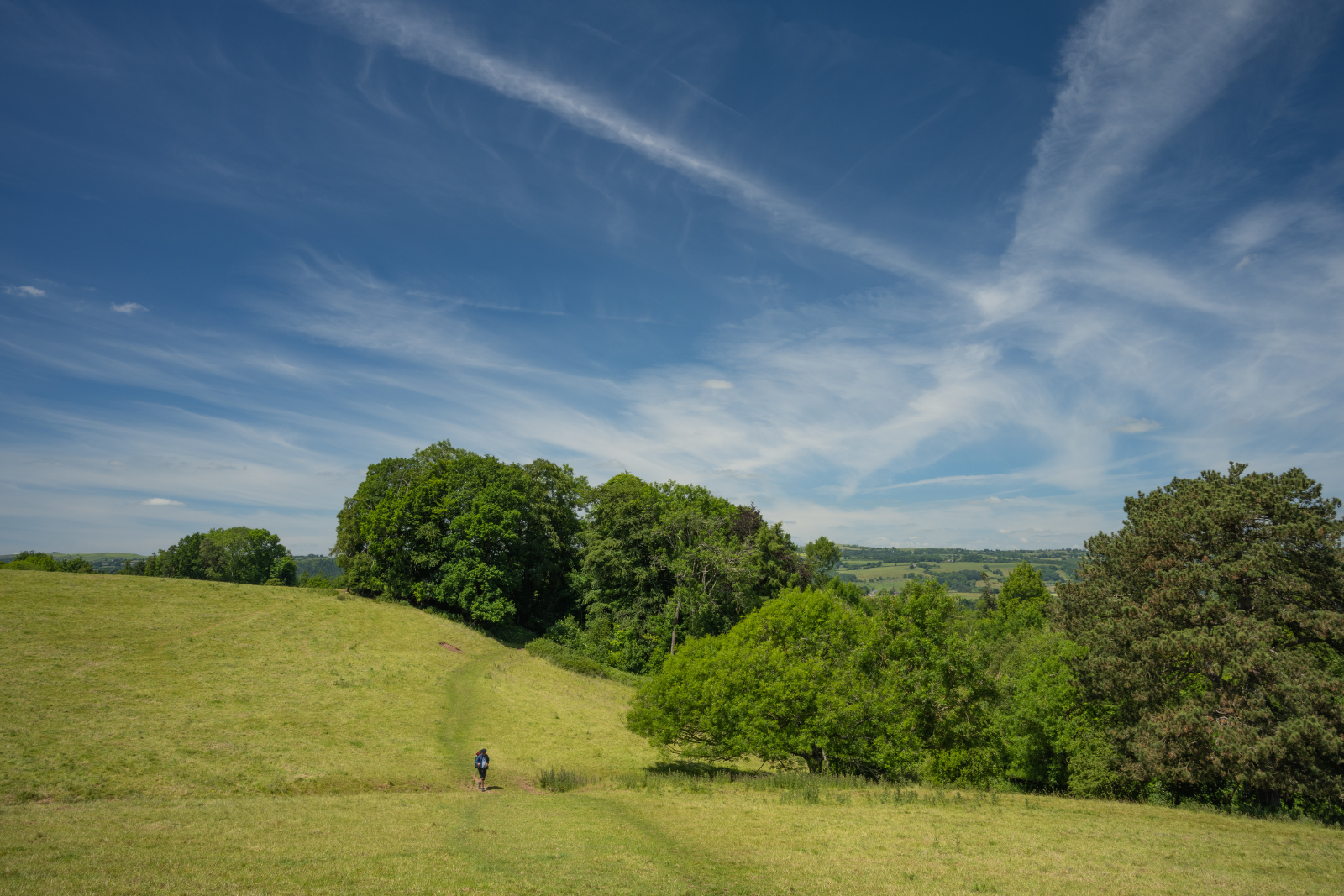 Walker crossing rolling countryside on Offa’s Dyke Path beneath a wide blue sky