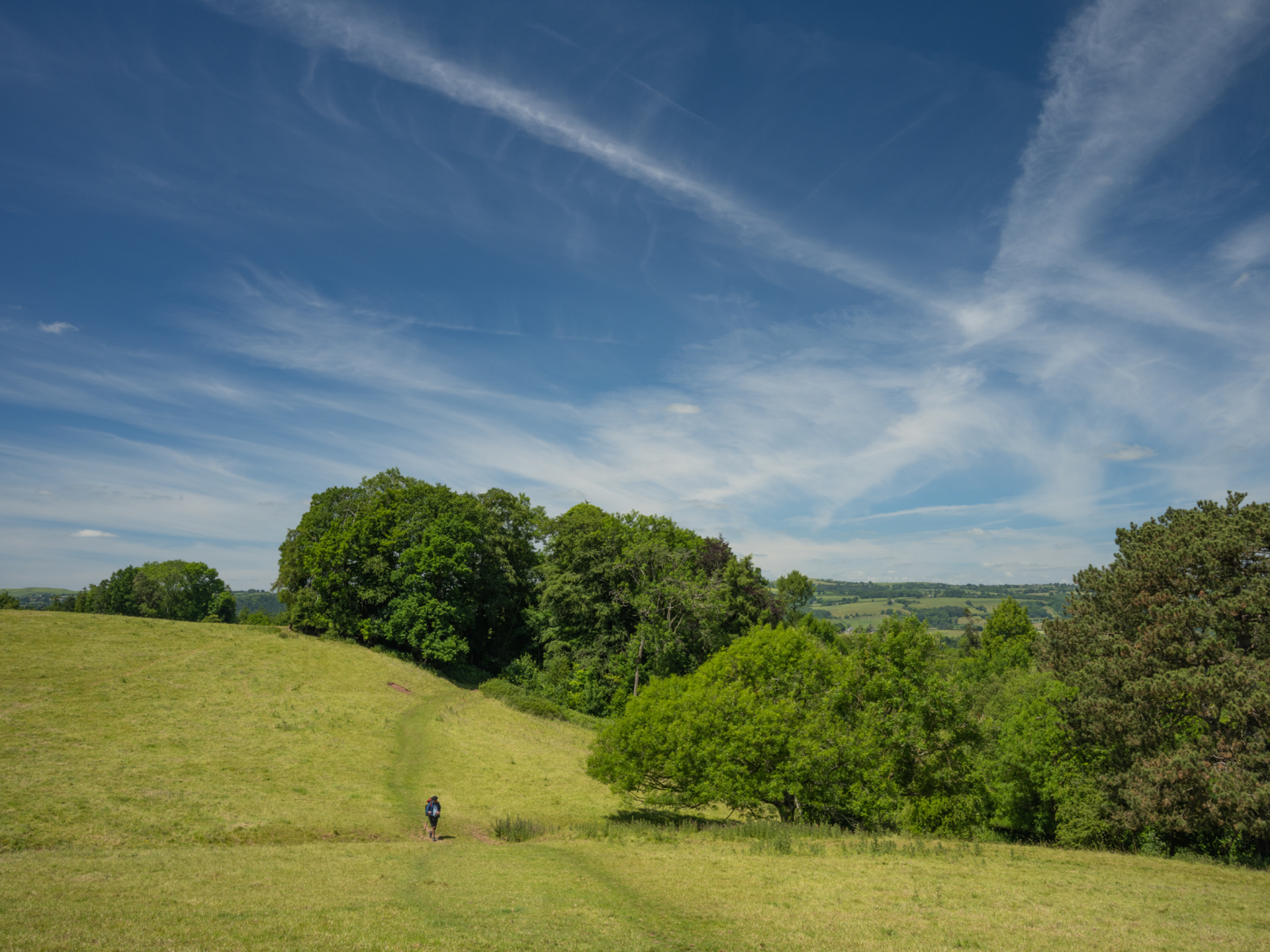 Walker crossing rolling countryside on Offa’s Dyke Path beneath a wide blue sky