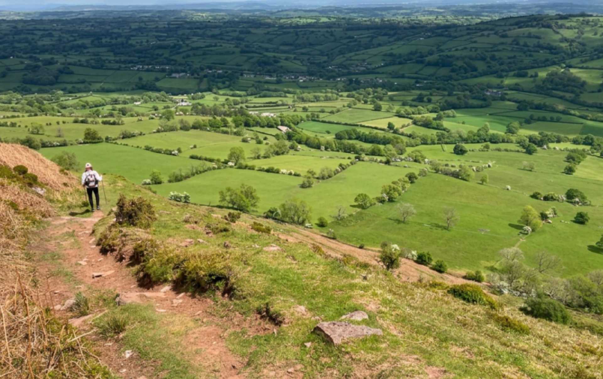 Walker descending from Hatterrall Ridge towards the patchwork fields near Hay-on-Wye.