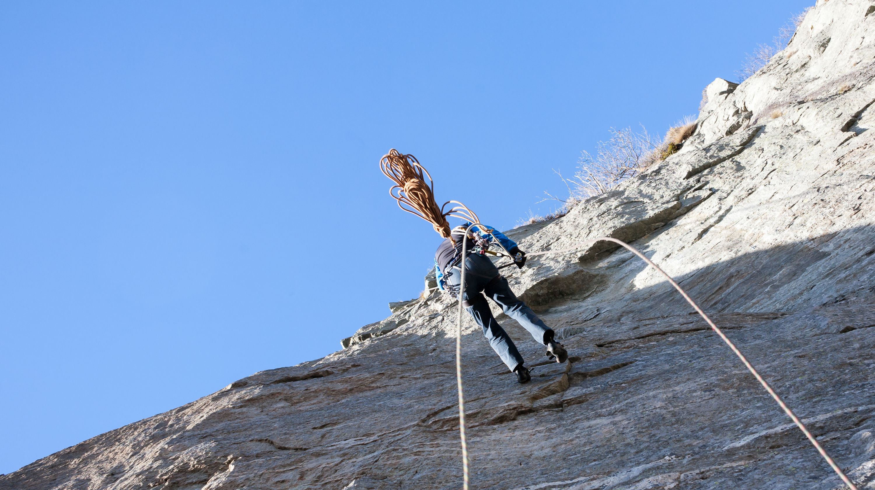 A person abseils down a sheer rock face with a long rope trailing behind them.