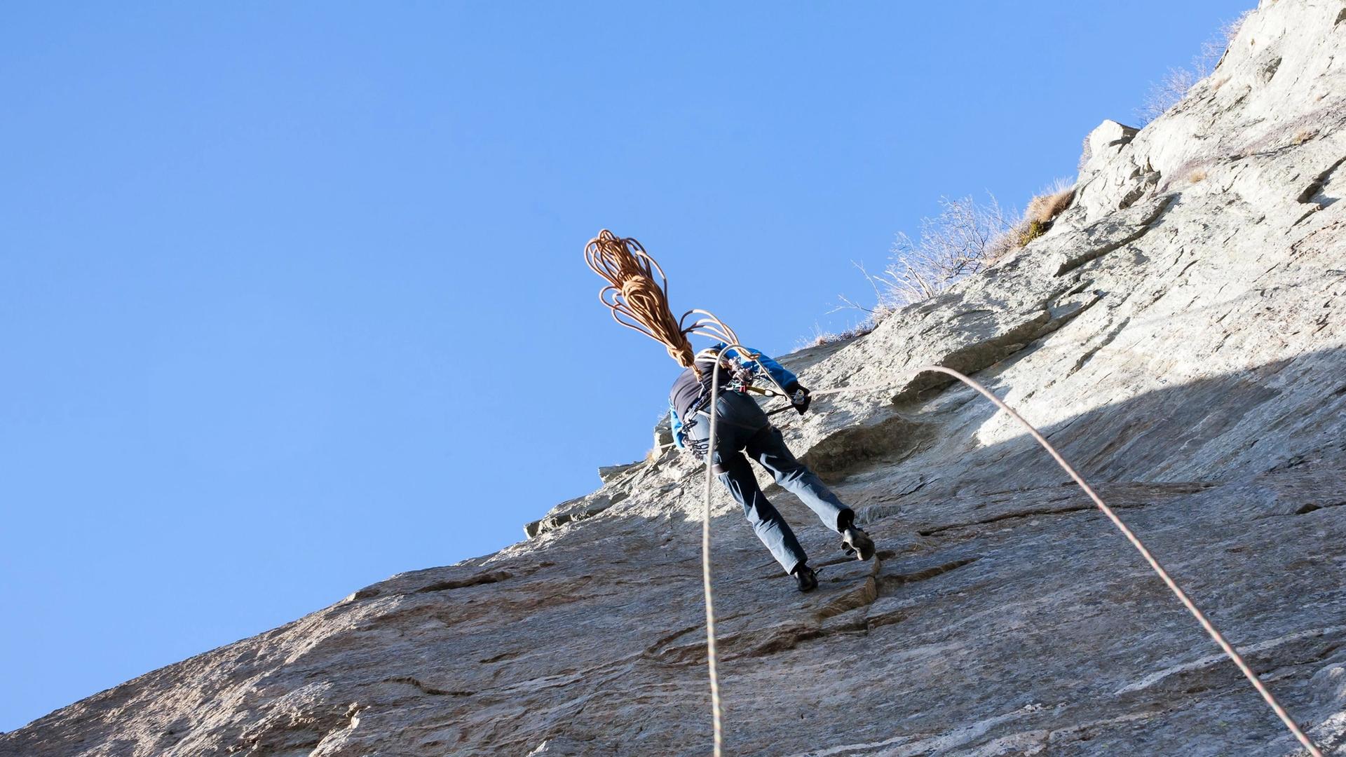 A person abseils down a sheer rock face with a long rope trailing behind them.