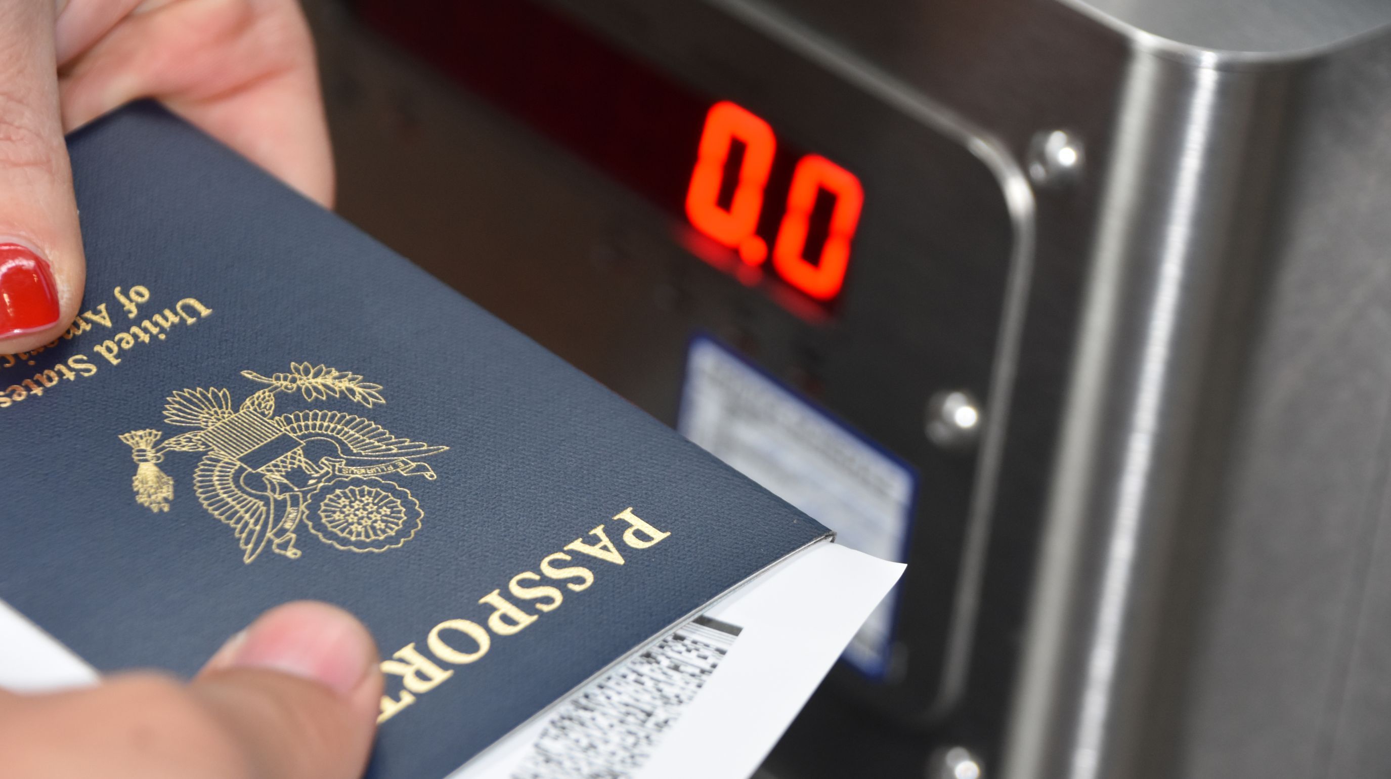 A hand holds a United States passport near a digital display showing "0.0".