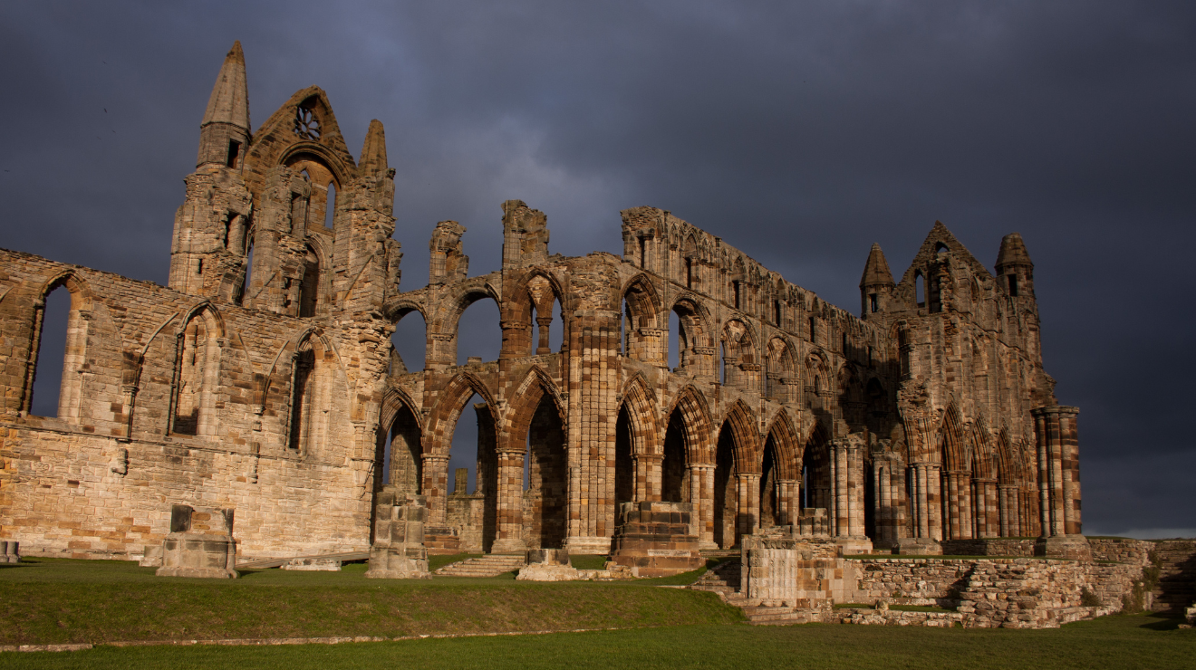 Sunlit ruins of Whitby Abbey beneath dark storm clouds on the Yorkshire coast.