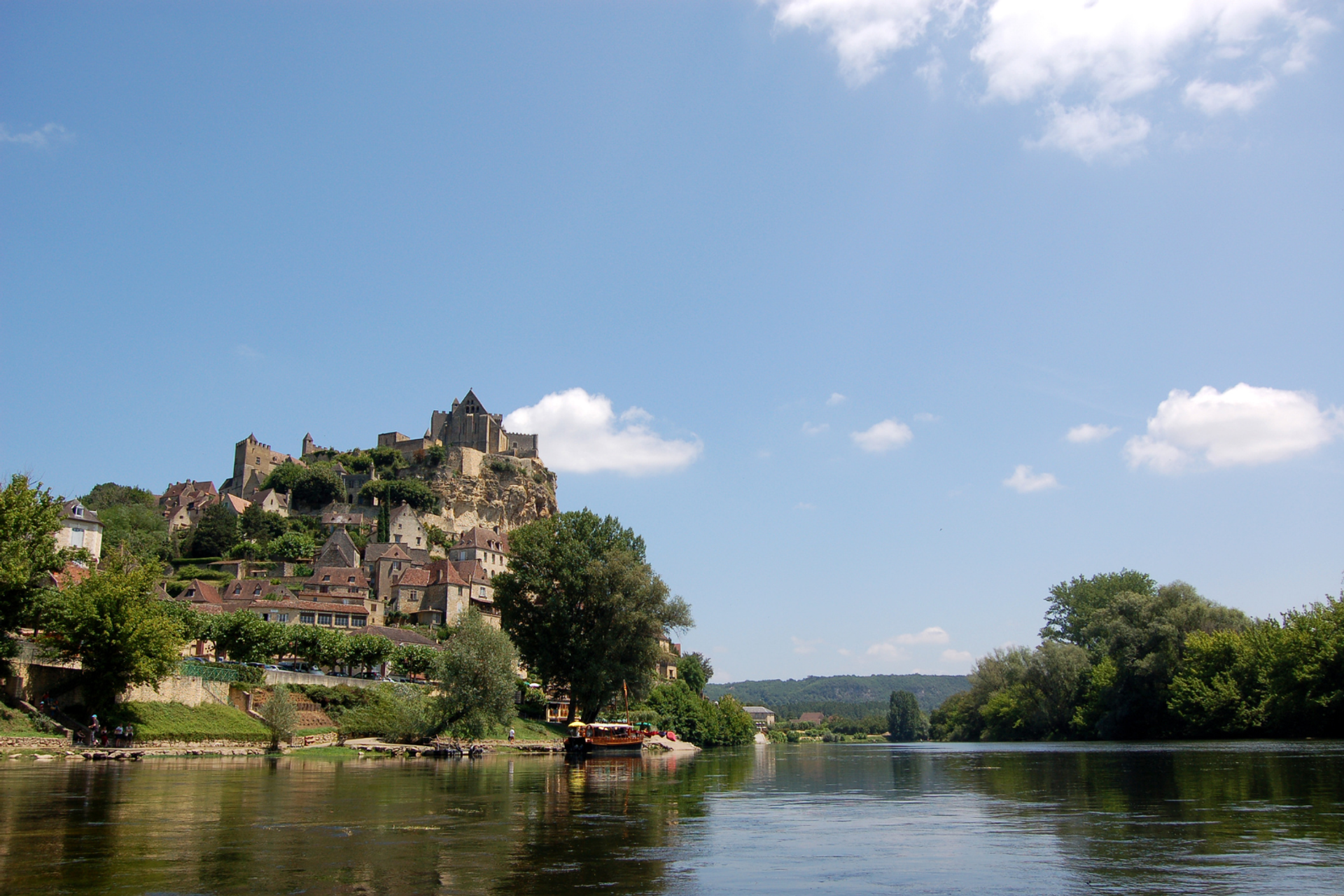 Medieval château and stone village perched above the Dordogne River, with wooded banks.
