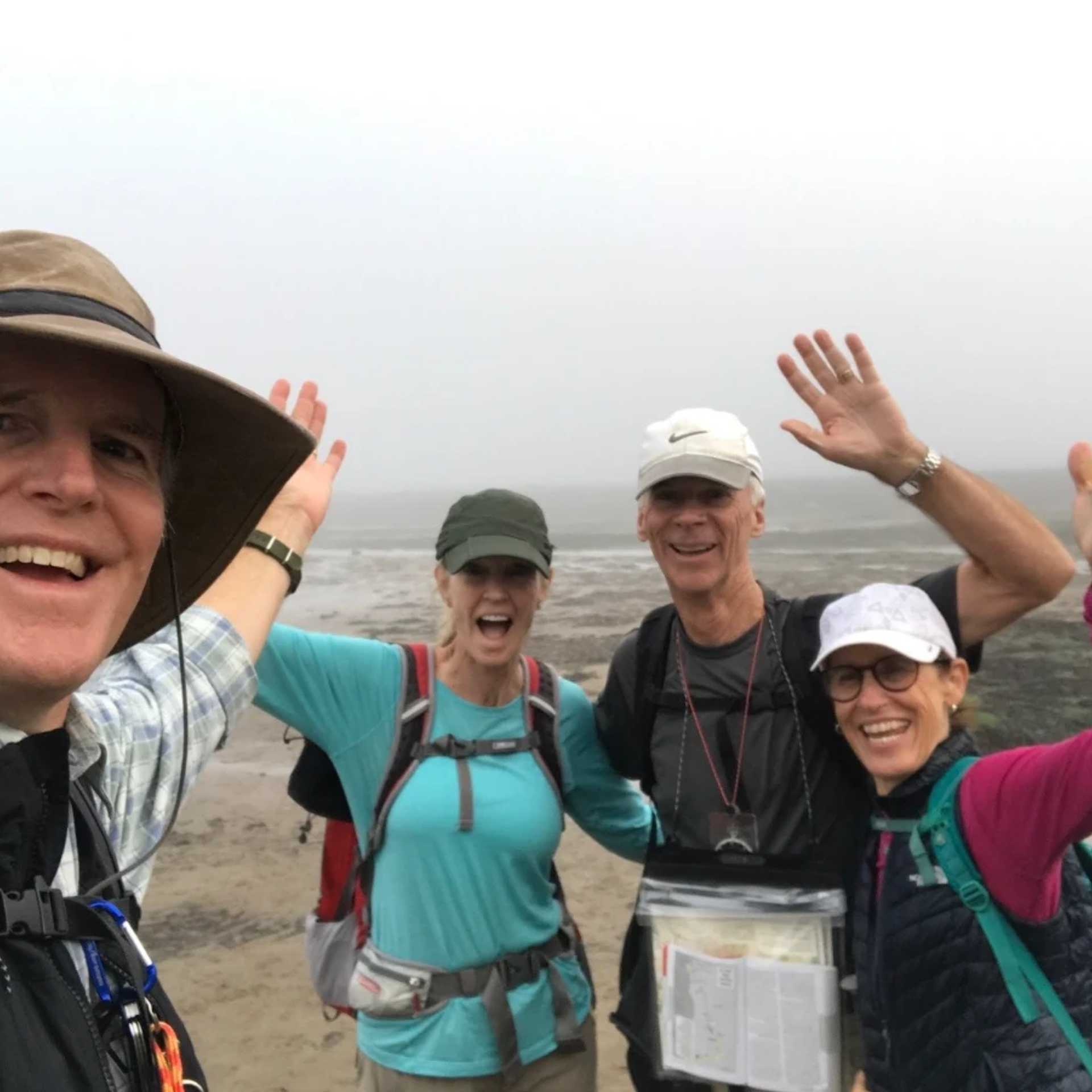 Group of walkers smiling and waving on a misty coastal walking trail.