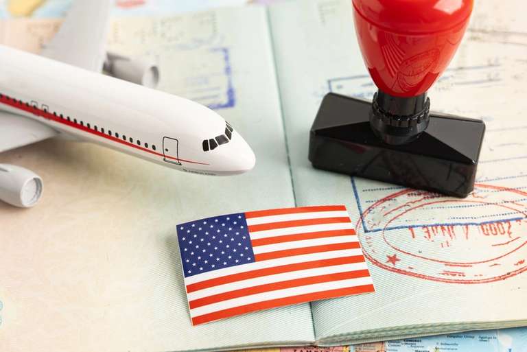 A toy airplane, a small American flag, and a red rubber stamp rest on an open passport with visa stamps.