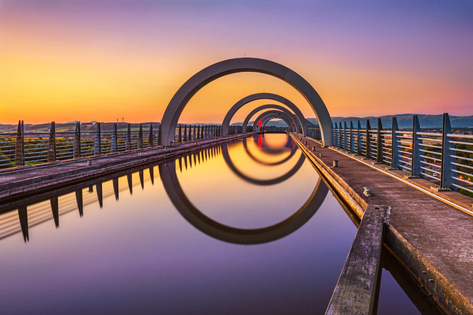 The Falkirk Wheel reflected in still water at sunset.
