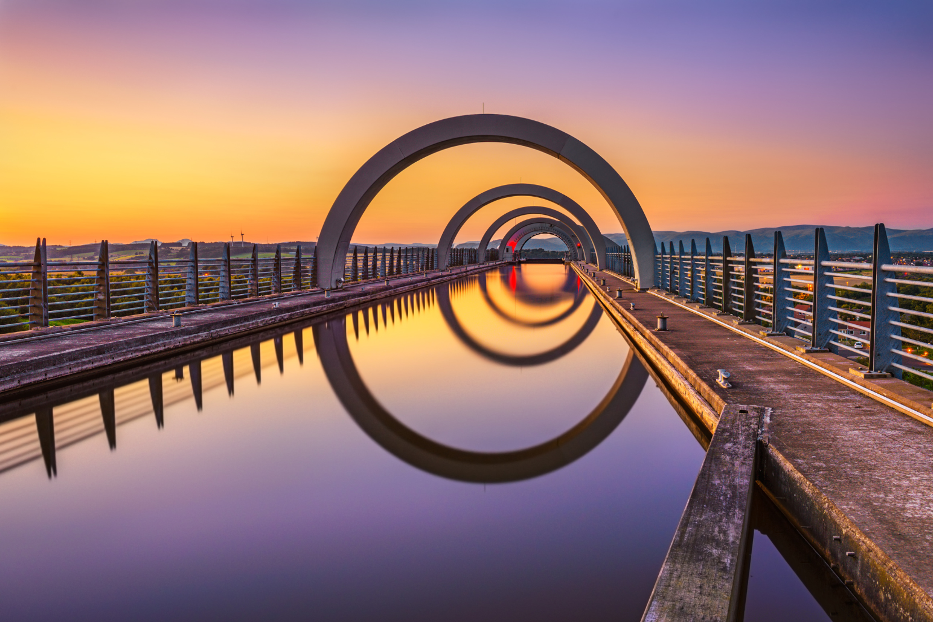 The Falkirk Wheel reflected in still water at sunset.