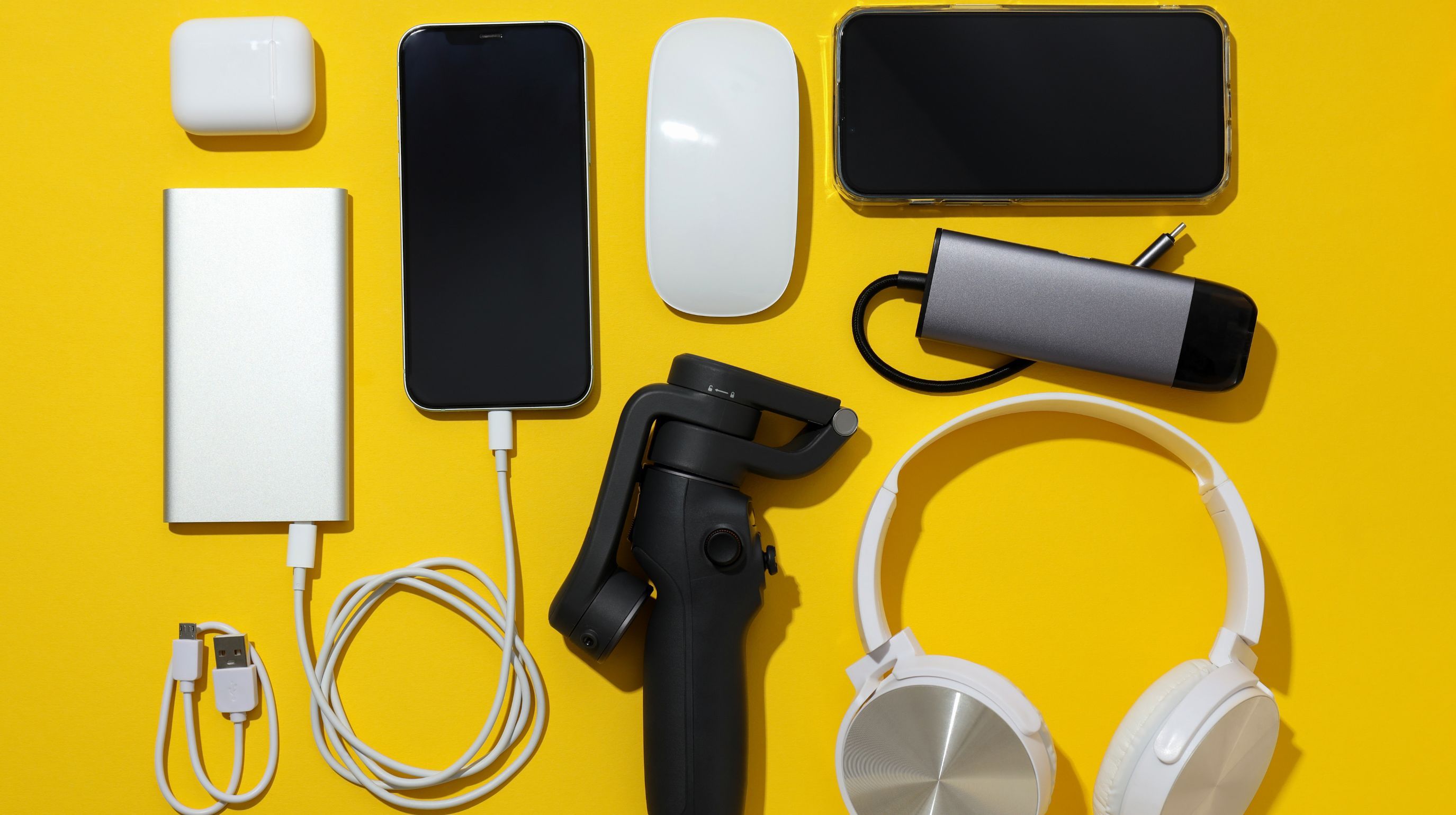 A collection of electronic gadgets, including a power bank, smartphone, wireless earbuds case, computer mouse, smartphone, USB hub, gimbal, and headphones, are arranged on a yellow background.