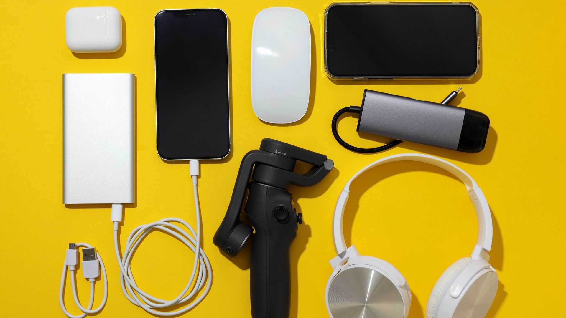 A collection of electronic gadgets, including a power bank, smartphone, wireless earbuds case, computer mouse, smartphone, USB hub, gimbal, and headphones, are arranged on a yellow background.