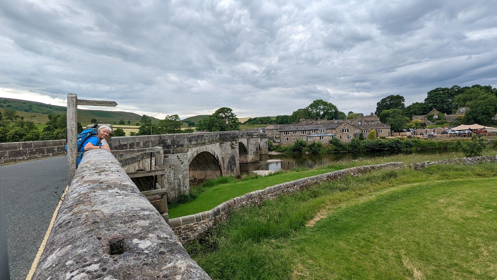 Walker crossing a historic stone bridge in the Yorkshire Dales on the Dales Way