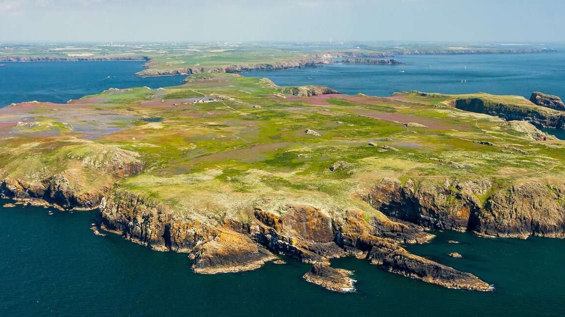 View from a plane of a small island surrounded by sea on a sunny day.