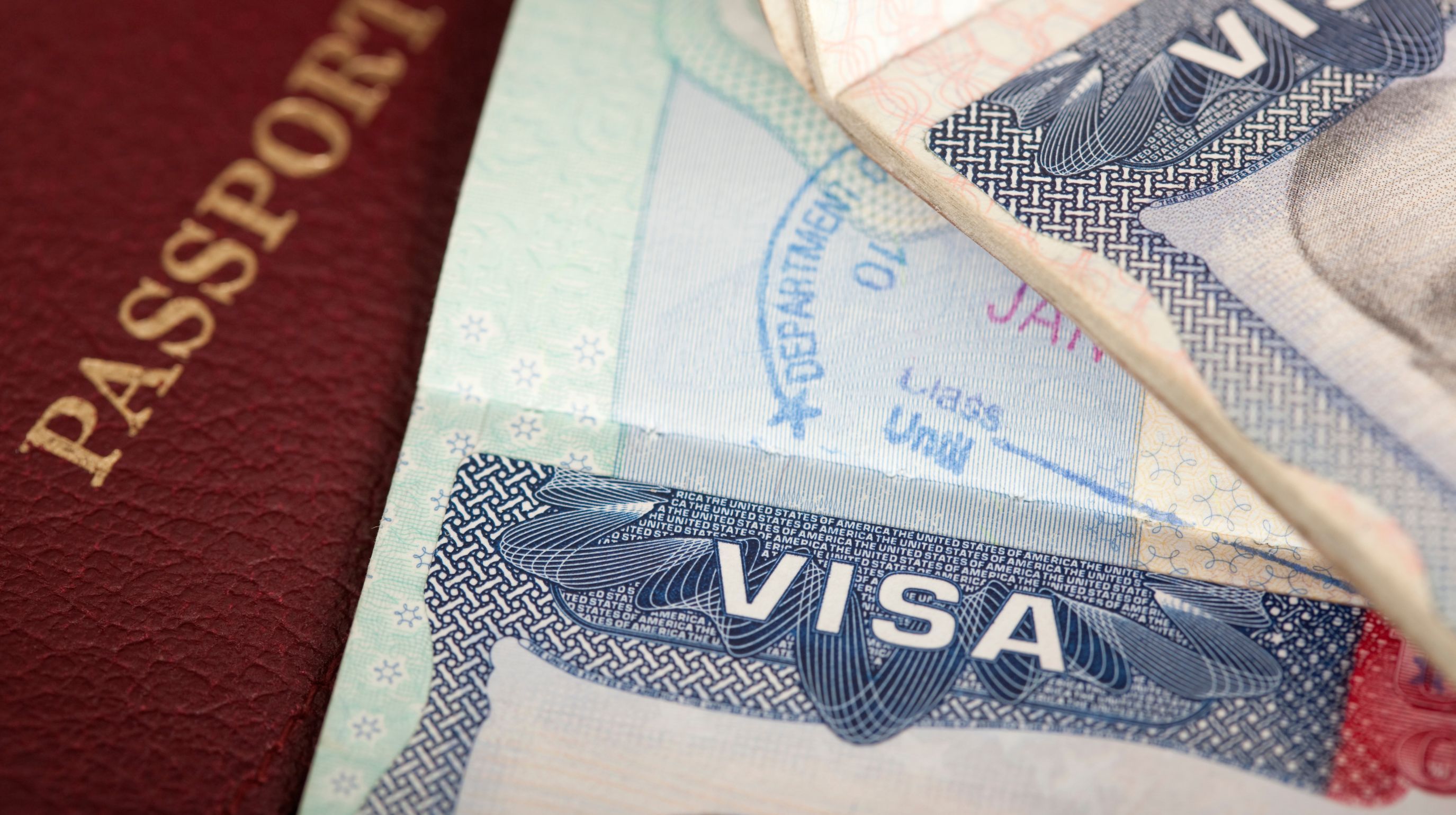 A close-up of a passport and a visa with a stamp that reads "DEPARTMENT OF STATE" and "JAN" and "Class Until"