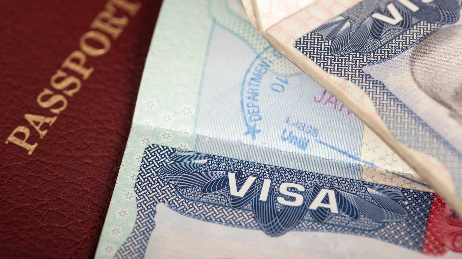 A close-up of a passport and a visa with a stamp that reads "DEPARTMENT OF STATE" and "JAN" and "Class Until"