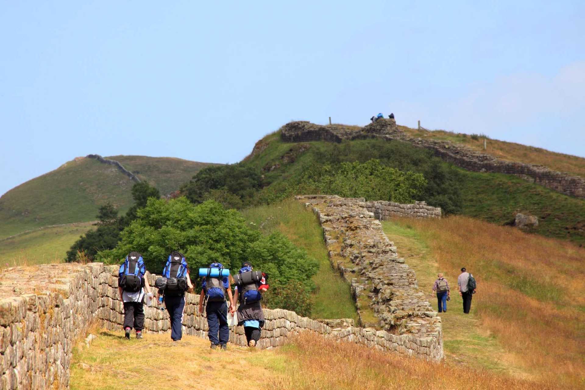Walkers with backpacks following Hadrian’s Wall across the Northumberland escarpment