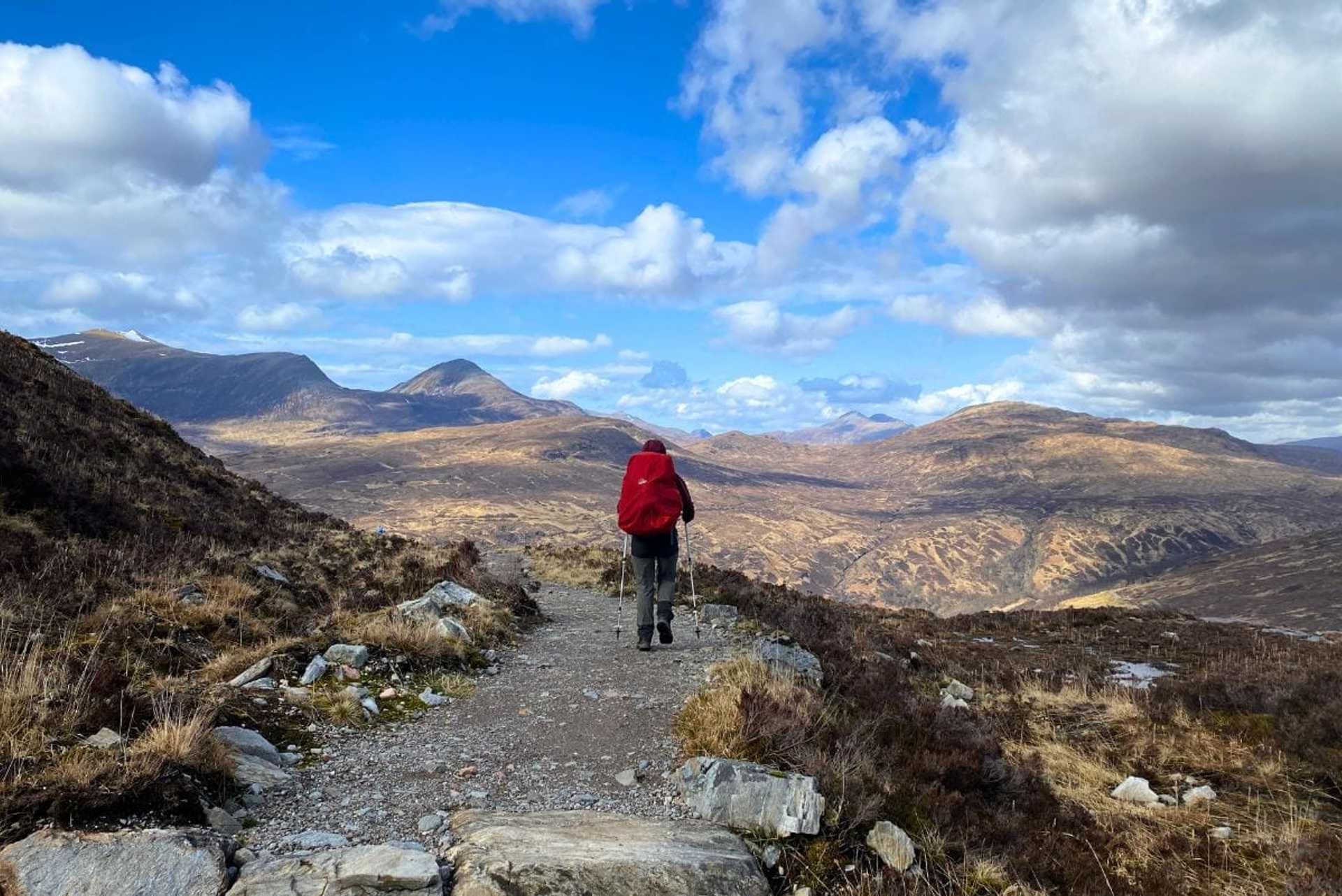 Walker on a Highland trail overlooking vast mountain scenery on the West Highland Way.