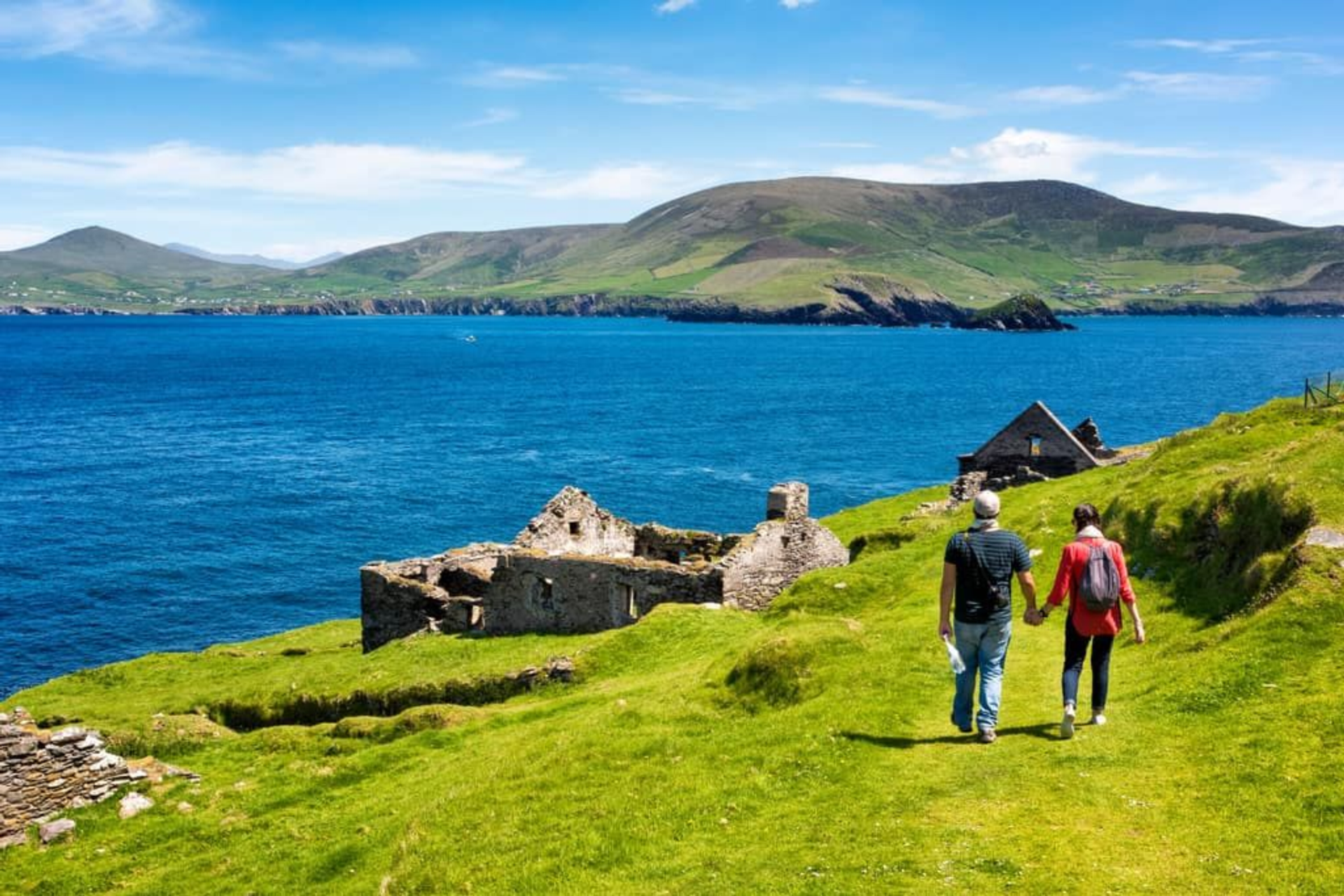 Two walkers passing stone ruins overlooking the coast and Blasket Islands on the Dingle Way