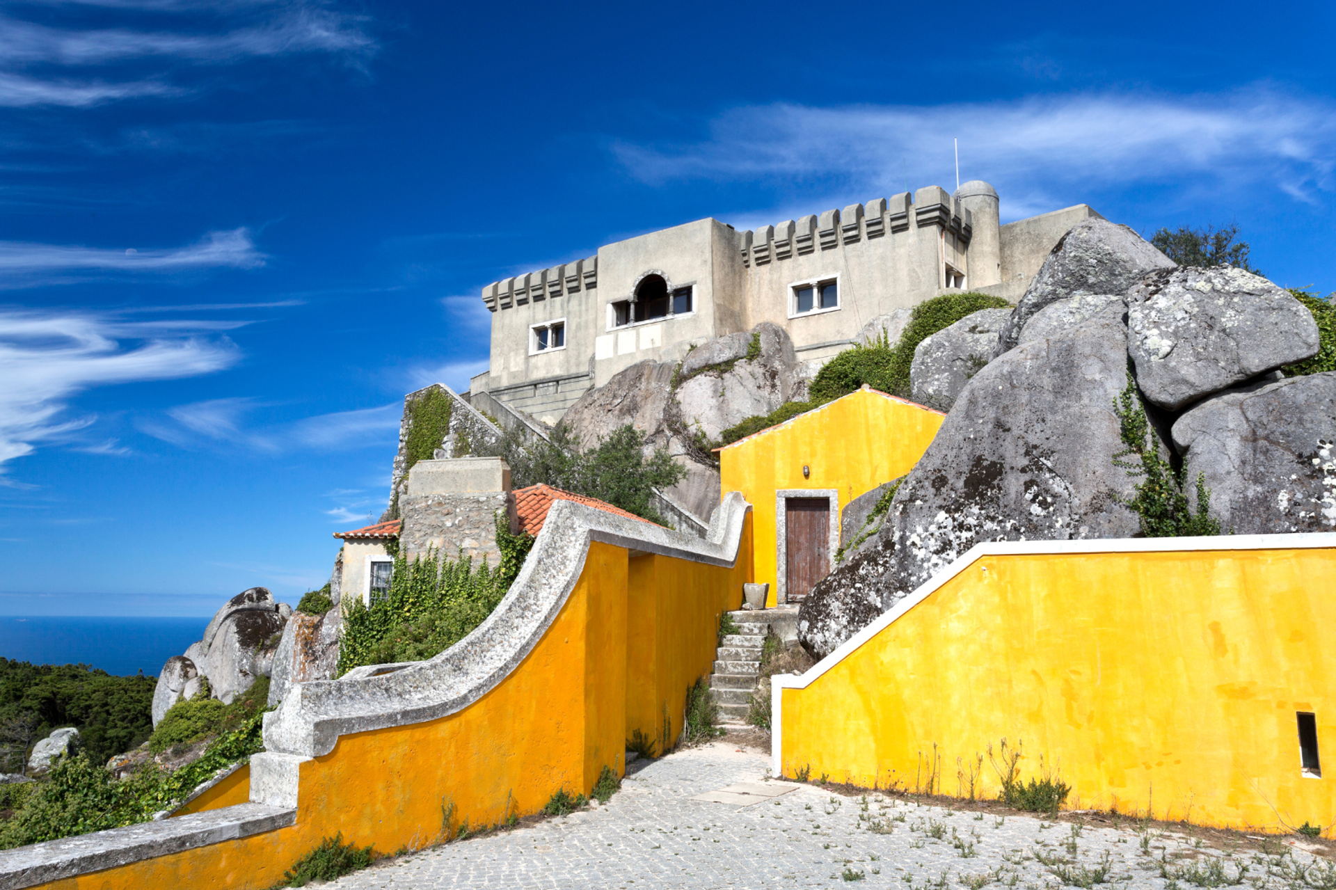 Yellow sanctuary walls and stone buildings among granite rocks at Peninha, Sintra.