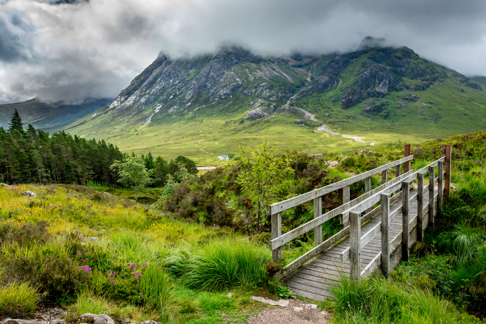 Wooden footbridge on the West Highland Way beneath cloud-covered mountains near Glencoe.
