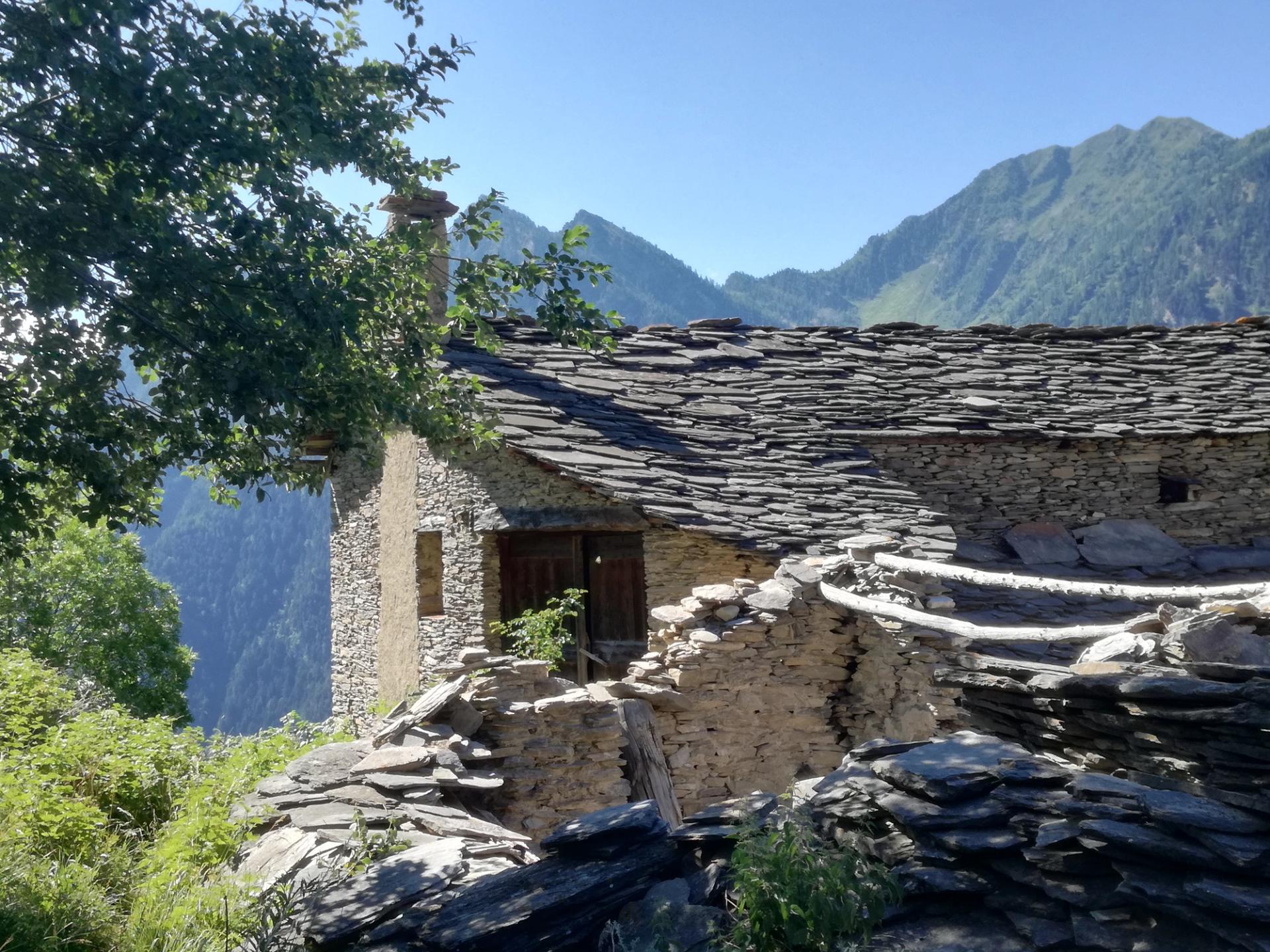 Traditional stone buildings with stone roofs against a backdrop of wooded mountains in Val Maira.