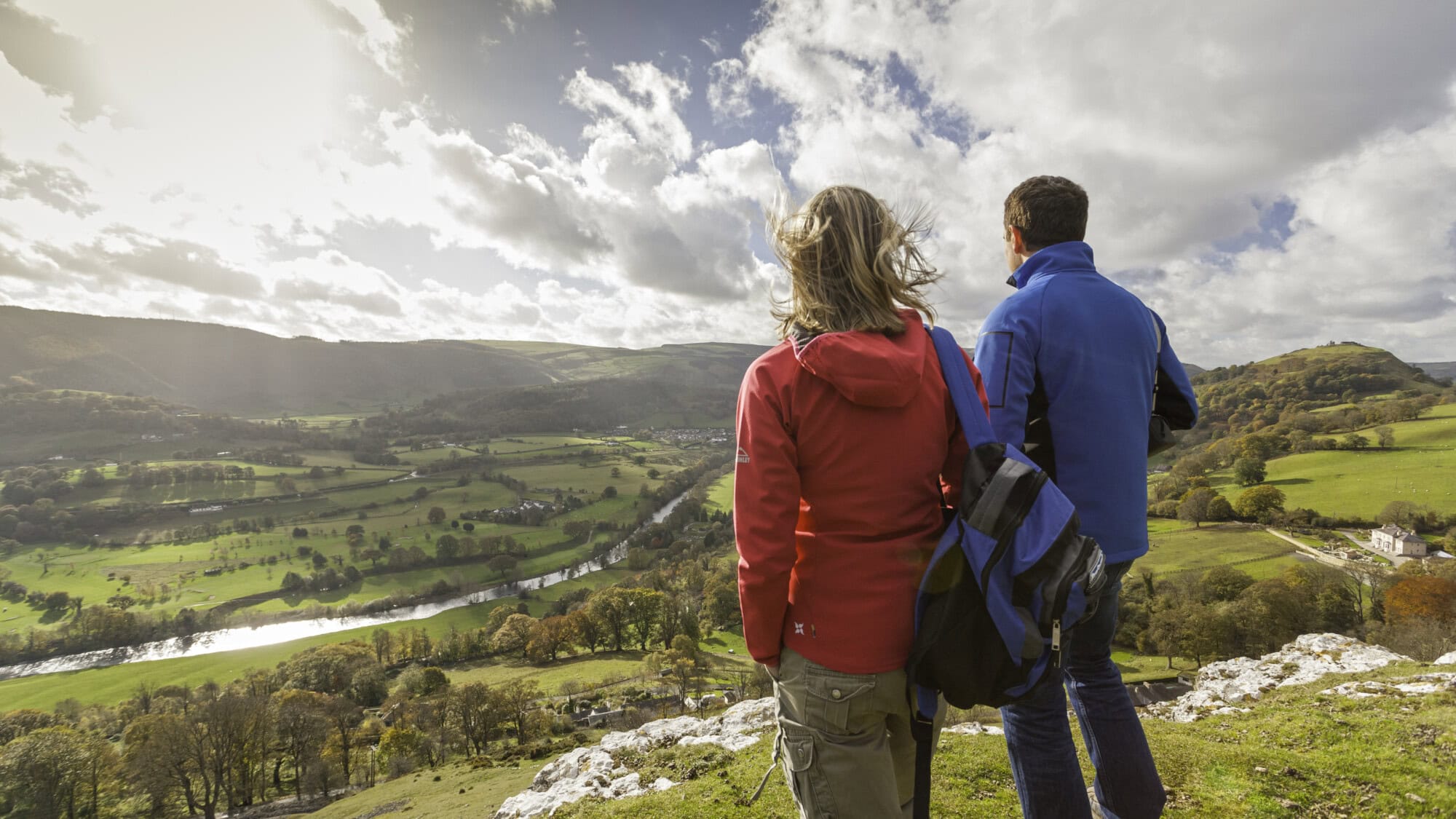 Two people looking out across a countryside valley, with green hills and a river.