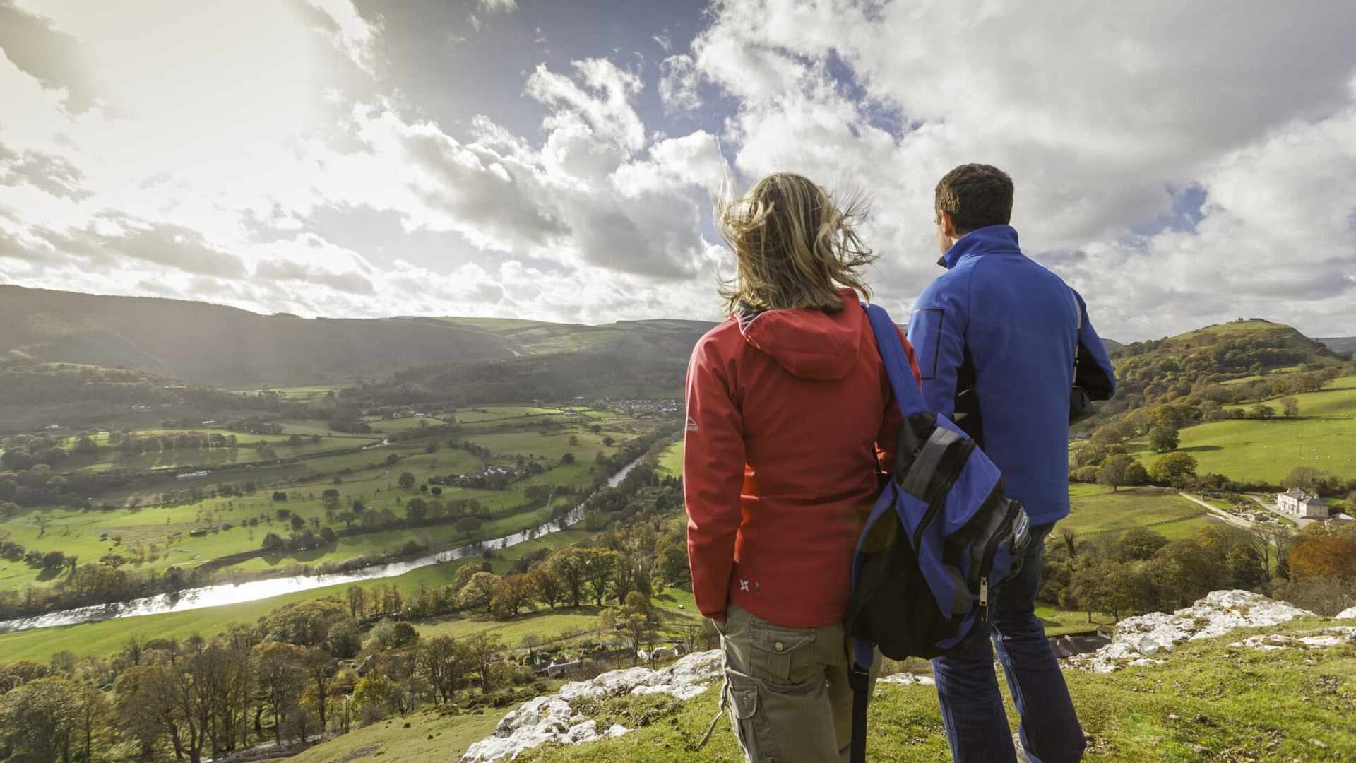 Two people looking out across a countryside valley, with green hills and a river.